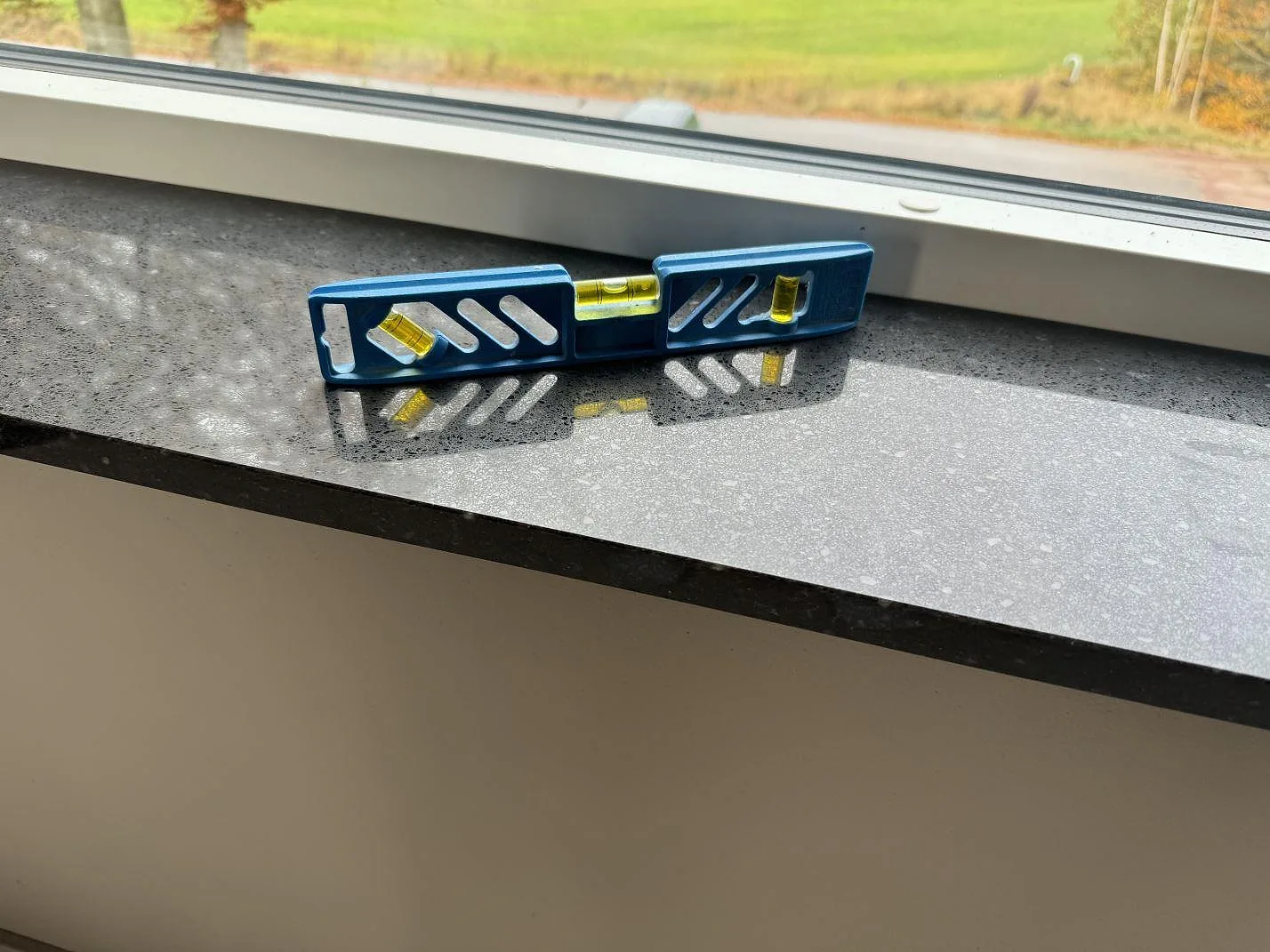 Närbild av polerad Silestone Arden Blue fönsterbänk med vattenpass som visar den mörka kompositytans spegling i Ängelholm.