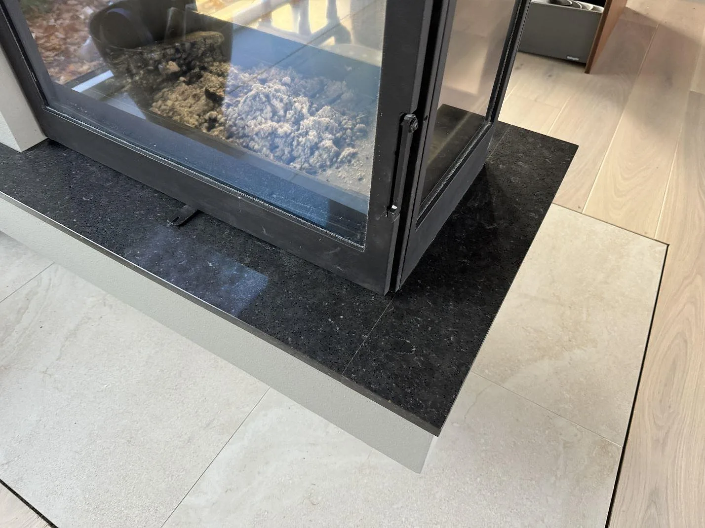 Eldstadsdetalj med polerad Silestone Arden Blue som mörk kompositskiva runt eldstadsinsatsen i Ängelholm.