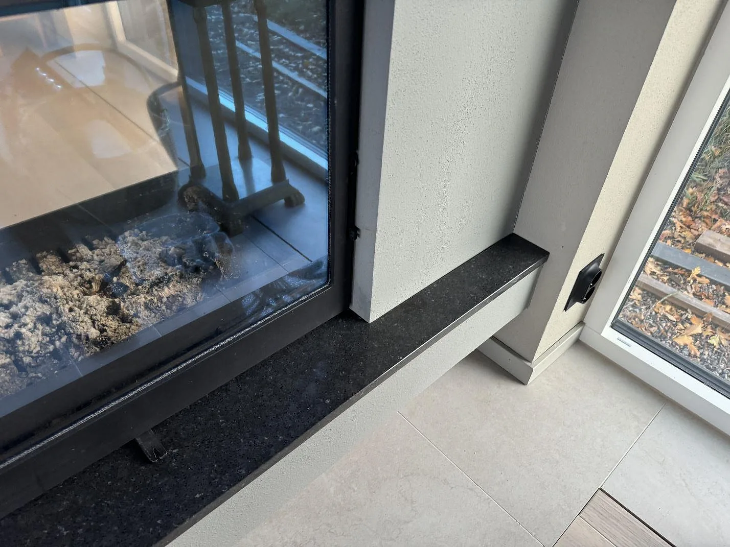 Eldstad med sidostycke i polerad Silestone Arden Blue och mörk kompositkant mot ljusa golv i Ängelholm.
