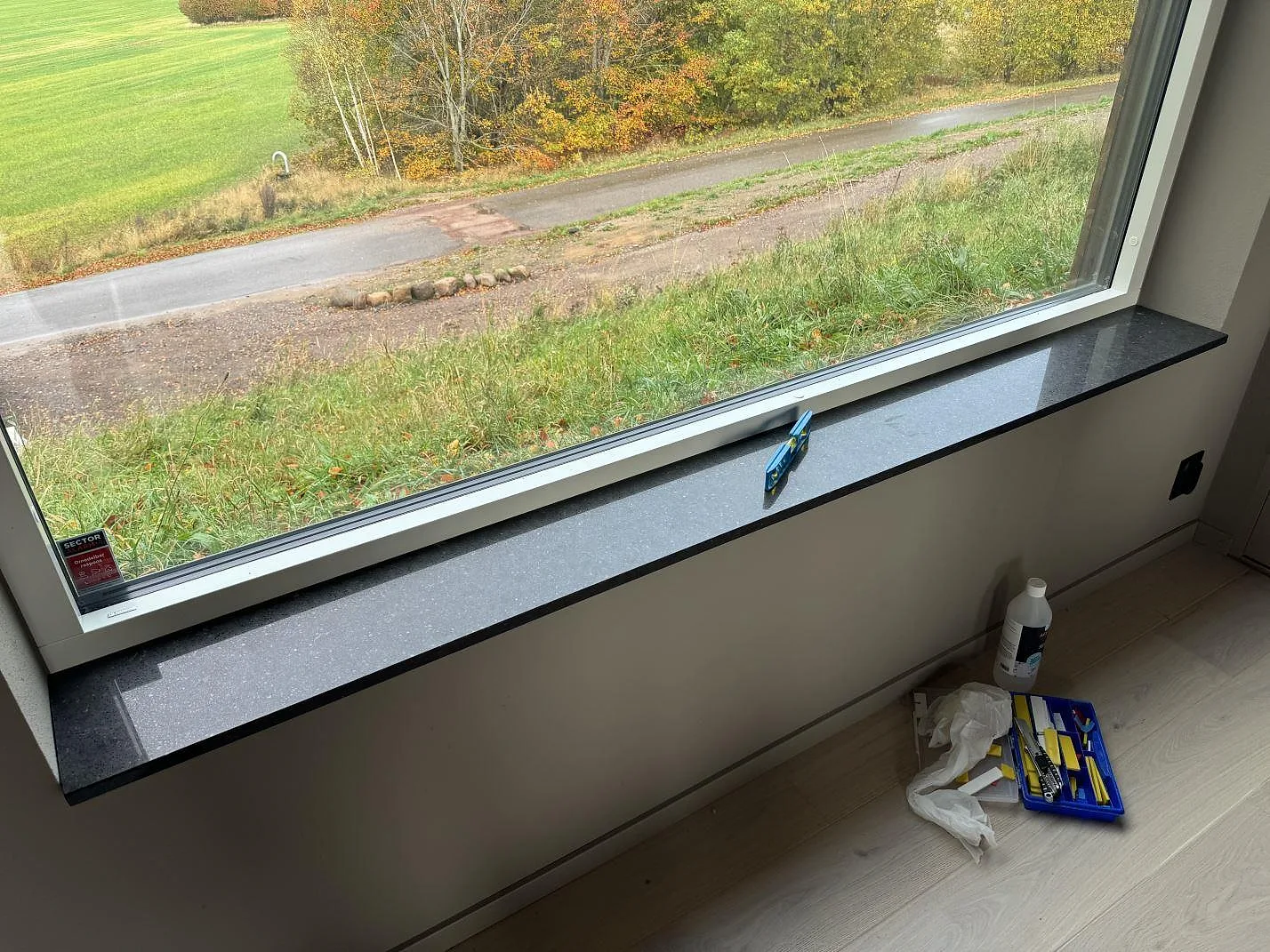 Bred fönsterbänk i polerad Silestone Arden Blue med blågrå komposityta och monteringsverktyg vid fönstret i Ängelholm.