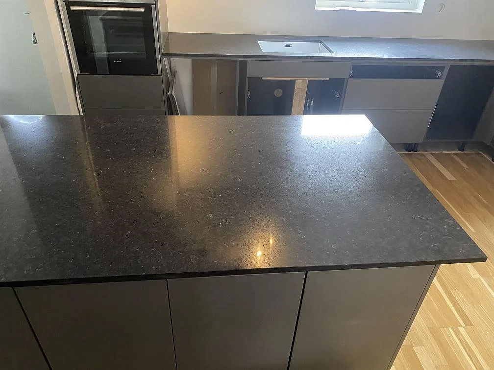 Stor köksö i polerad Silestone Arden Blue med mörka köksstommar och väggbänkar i ett kök i Nättraby.
