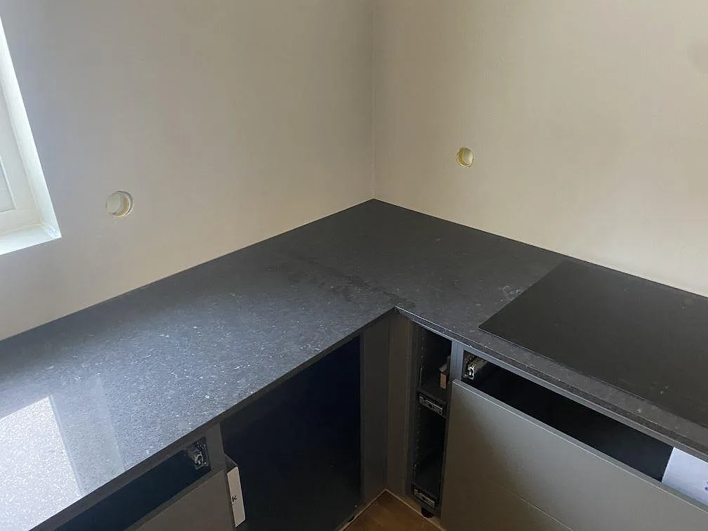 L-formad bänkskiva i polerad Silestone Arden Blue med häll och mörka underskåp i ett kök i Nättraby.