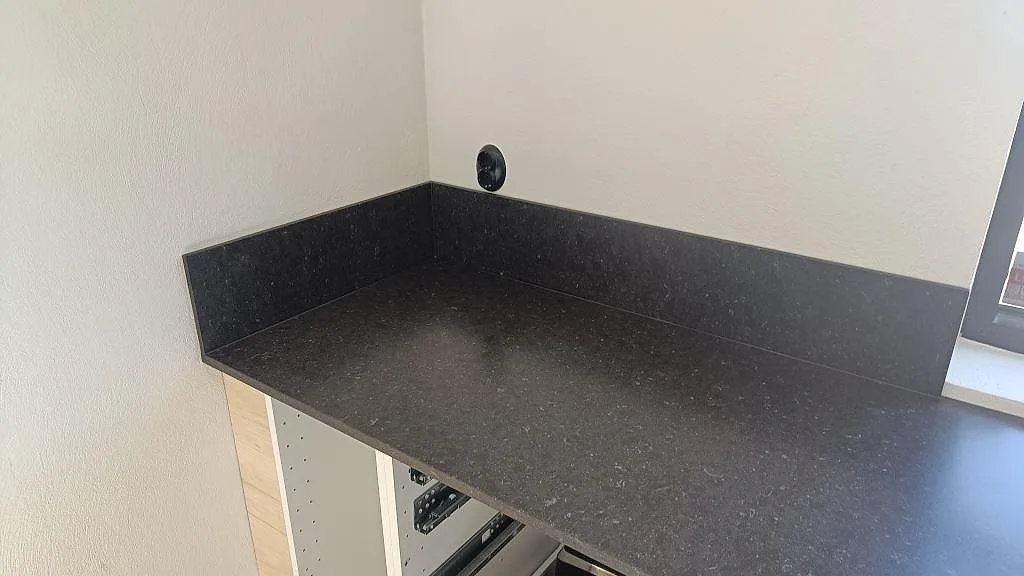 Bänkskiva i Silestone Arden Blue med låg stänkkant i samma mörka kvartskomposit vid fönsterväggen i Smedstorp.