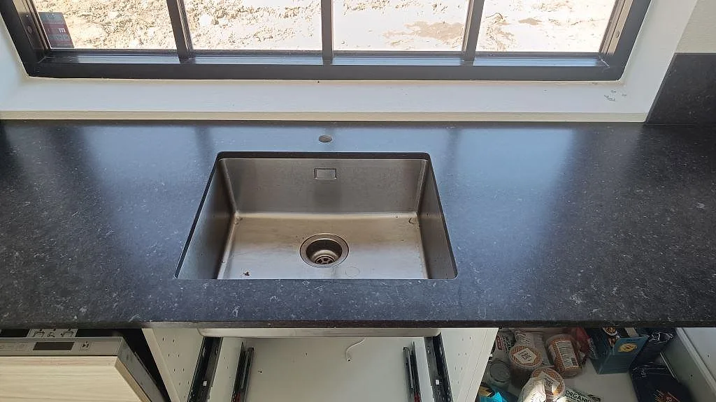 Diskhozonen i Silestone Arden Blue med mörk matt komposityta, rostfri ho och fönsterläge i Smedstorp.