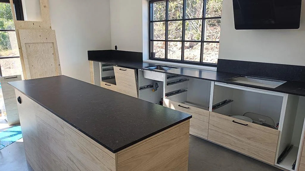 Köksbänkskiva och köksö i mörkt Silestone Arden Blue, matt Mocka, med stänkskydd och öppningar för diskho och häll i ett kök i Smedstorp.