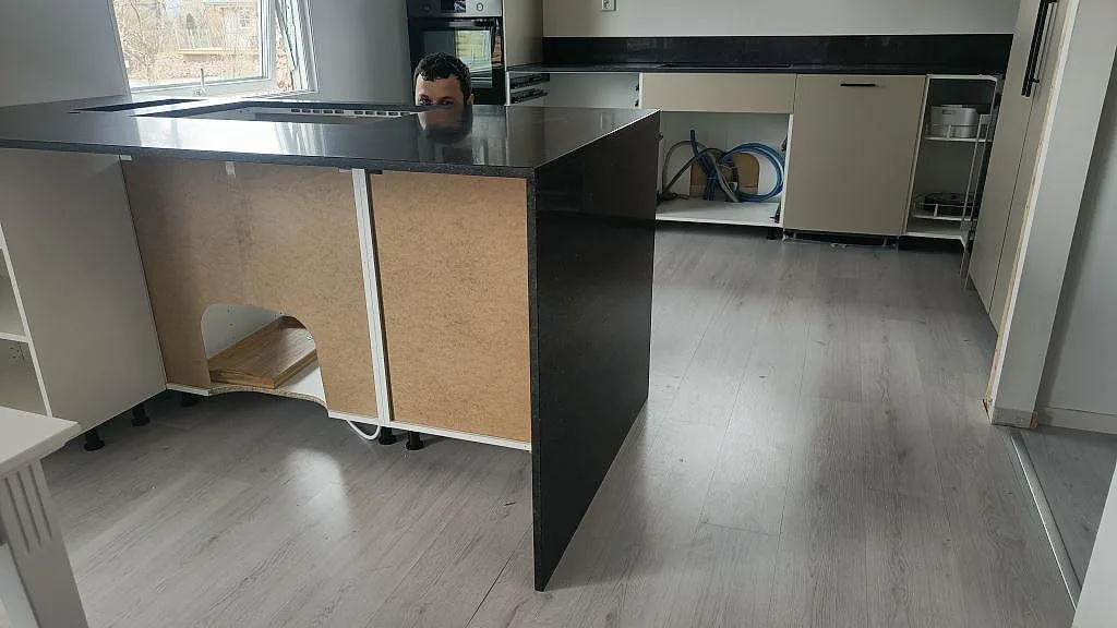 Köksö i blågrå Silestone Arden Blue med waterfall-gavel och öppna stommar under montering i ett kök i Torslanda.