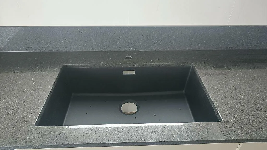 Underlimmad antracitfärgad kompositdiskho monterad under bänkskivan i Silestone Arden Blue i ett kök i Torslanda.