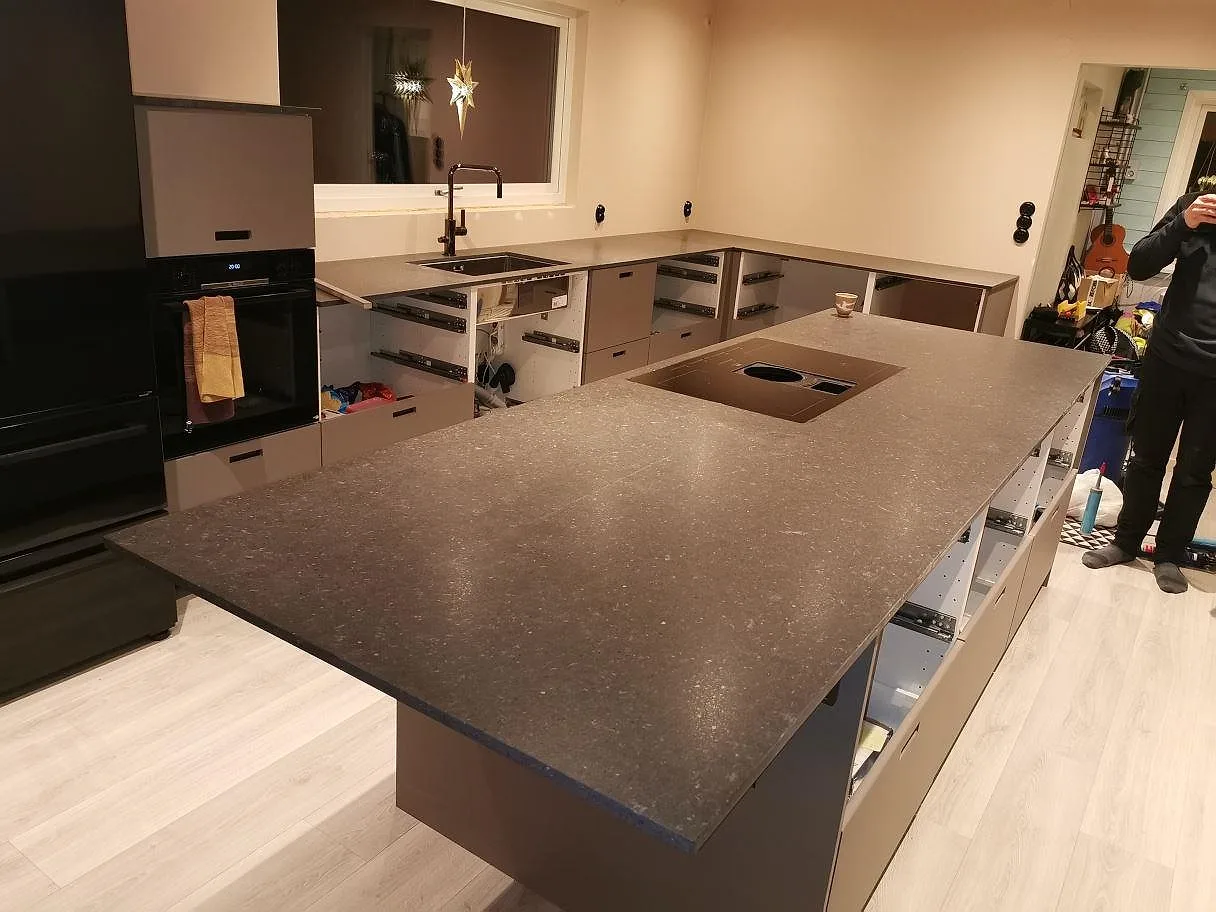 Köksbänkskiva i Silestone Arden Blue, mörkt blågrå kvartskomposit i matt Mocka-finish, med köksö och underlimmad rostfri diskho i ett kök under montering i Varberg.