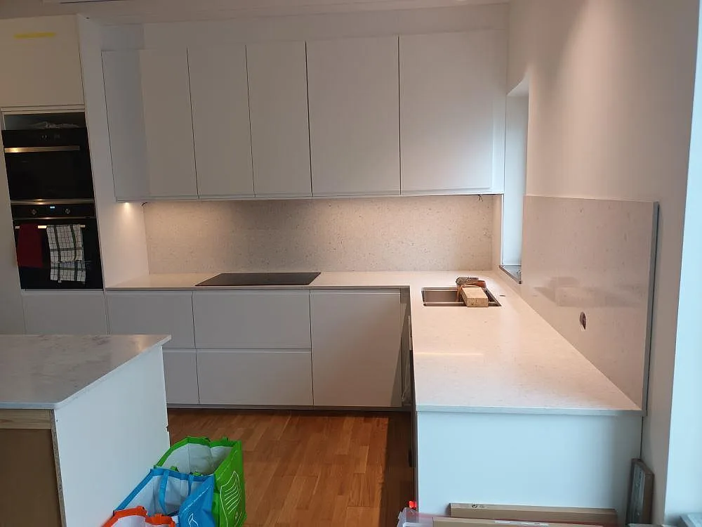 Köksbänkskiva i ljus Silestone Bianco River, polerad, med underlimmad diskho och infälld induktionshäll i ett U-format kök i Lidingö.
