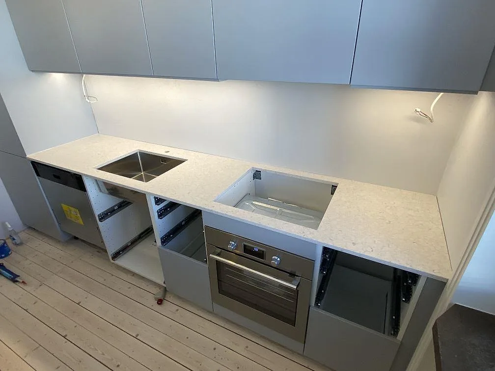 Köksbänkskiva i vit Silestone Bianco River, matt kvartskomposit med grå ådring, i en lång köksrad med underlimmad rostfri diskho och förberedd hällurtagning i ett kök i Malmö.