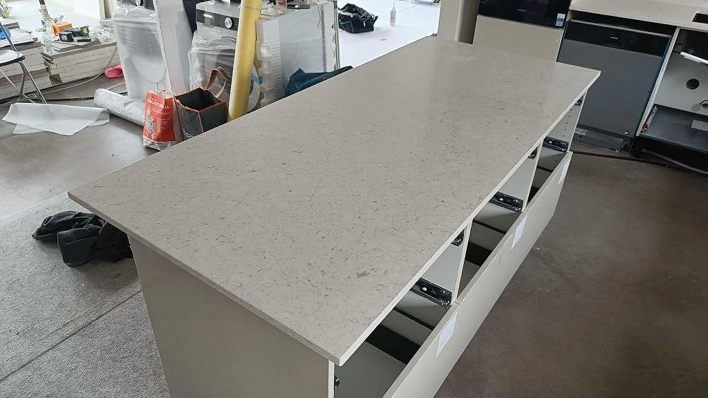 Stor köksö med polerad Silestone Bianco River i vit komposit under montering i ett kök i Ytterby.