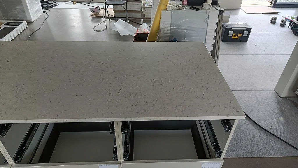 Närbild på köksö i polerad Silestone Bianco River med ljus ådring och öppna lådstommar i Ytterby.
