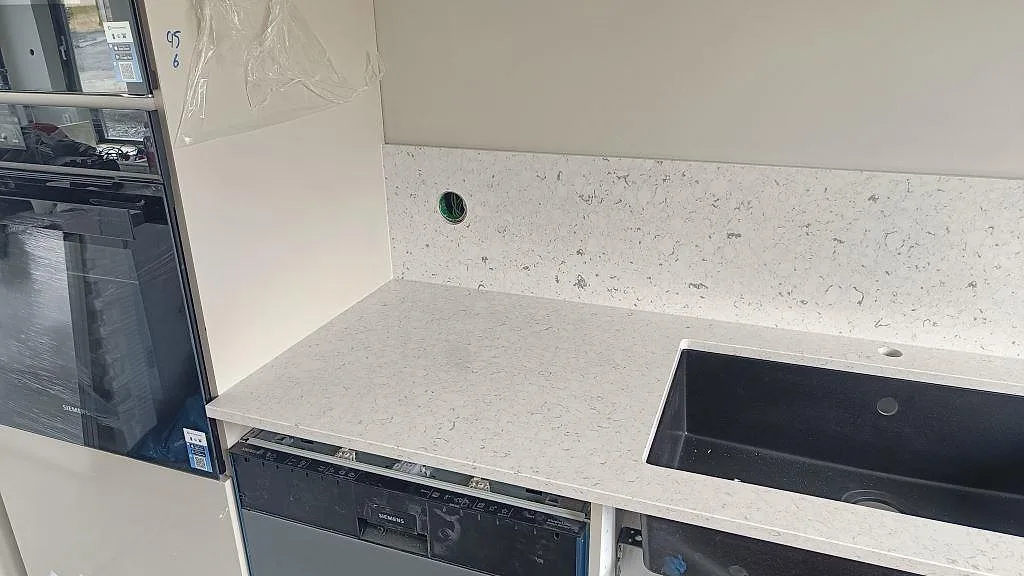 Köksbänkskiva i Silestone Bianco River med svart underlimmad diskho, diskmaskin och stänkskydd i Ytterby.