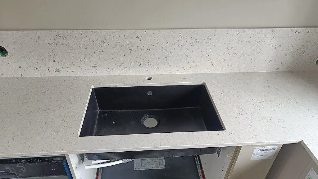 Svart underlimmad diskho i polerad Silestone Bianco River med matchande stänkskydd i kök i Ytterby.