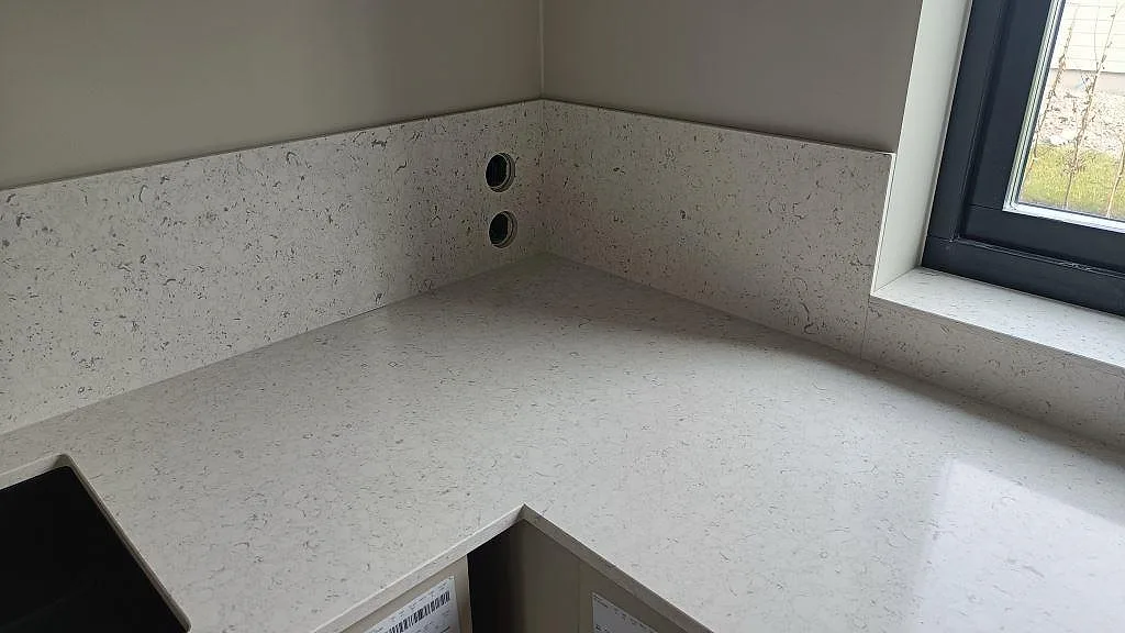Hörndel av köksbänkskiva i Silestone Bianco River med stänkskydd och fönsternisch i Ytterby.