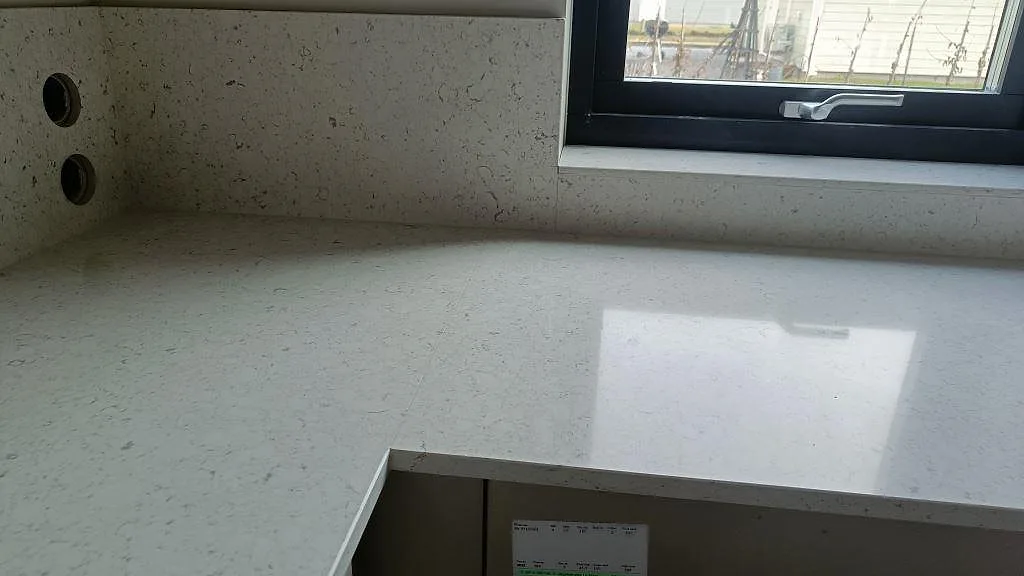 Polerad bänkskiva i Silestone Bianco River vid fönster med ljus reflektion och stänkskydd i Ytterby.