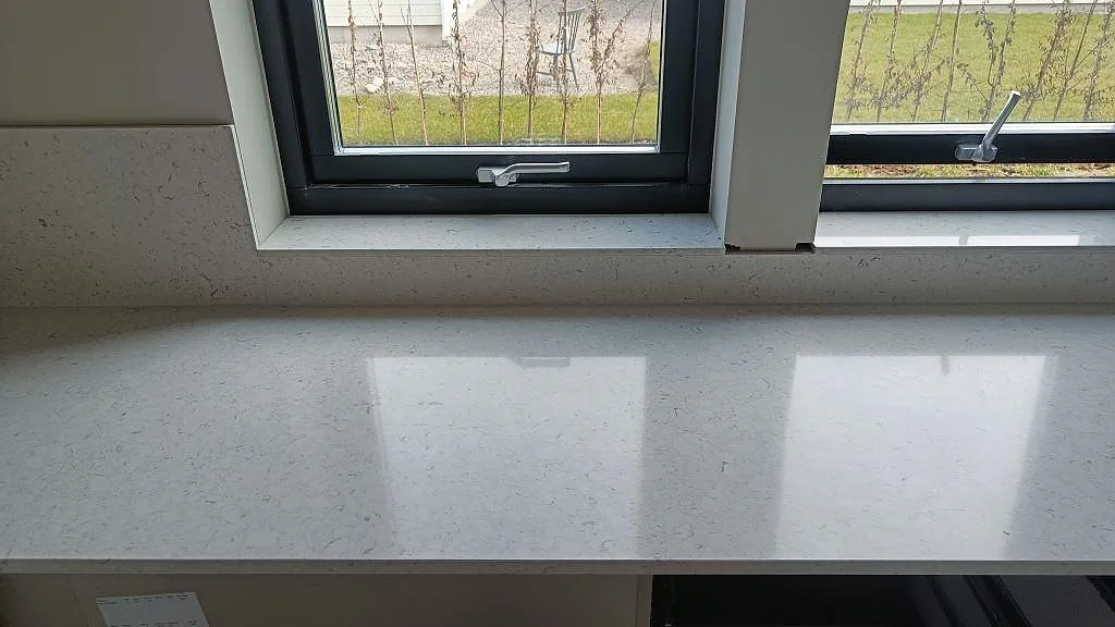 Lång köksbänkskiva i vit Silestone Bianco River, polerad, under fönster i ett kök i Ytterby.