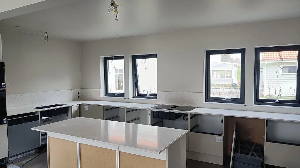 Köksbänkskiva i vit Silestone Bianco River, polerad komposit, med stor köksö, stänkskydd och svarta fönster i Ytterby.