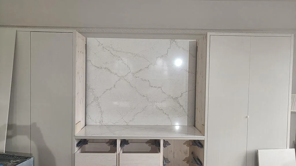Väggpanel och bänkskiva i polerad Silestone Blanc Elysee, vit kvartskomposit med grå ådring vid köksförvaring i Allerum.