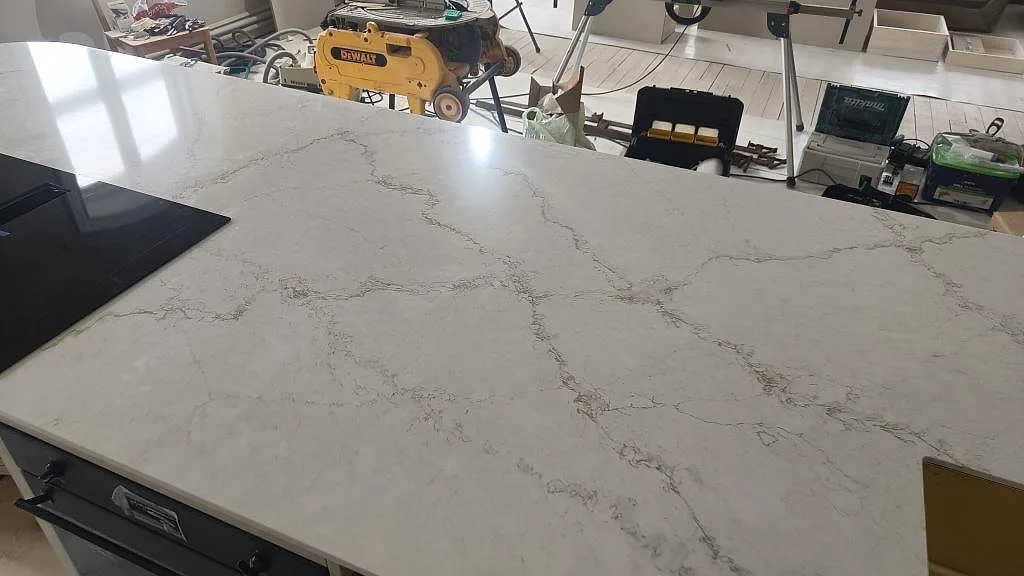 Ytbild av polerad Silestone Blanc Elysee på köksö, med synlig ådring, häll och diskho som detaljer i Allerum.
