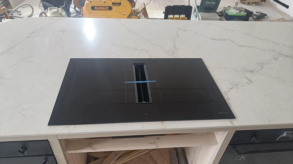Närbild på svart häll monterad i polerad Silestone Blanc Elysee, vit kompositbänkskiva med grå ådring i Allerum.