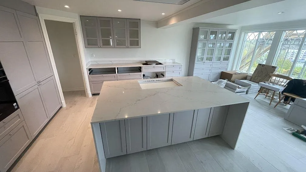 Köksbänkskiva och stor köksö i vit Silestone Blanc Elysee, polerad, med grå ådring och urtag för diskho i ett ljust kök under montering i Strömstad.