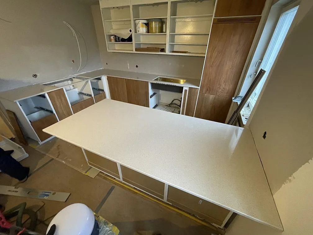 Polerad köksö i Silestone Blanco City med L-formad bänkskiva bakom i ett kök under montering i Hässelby.