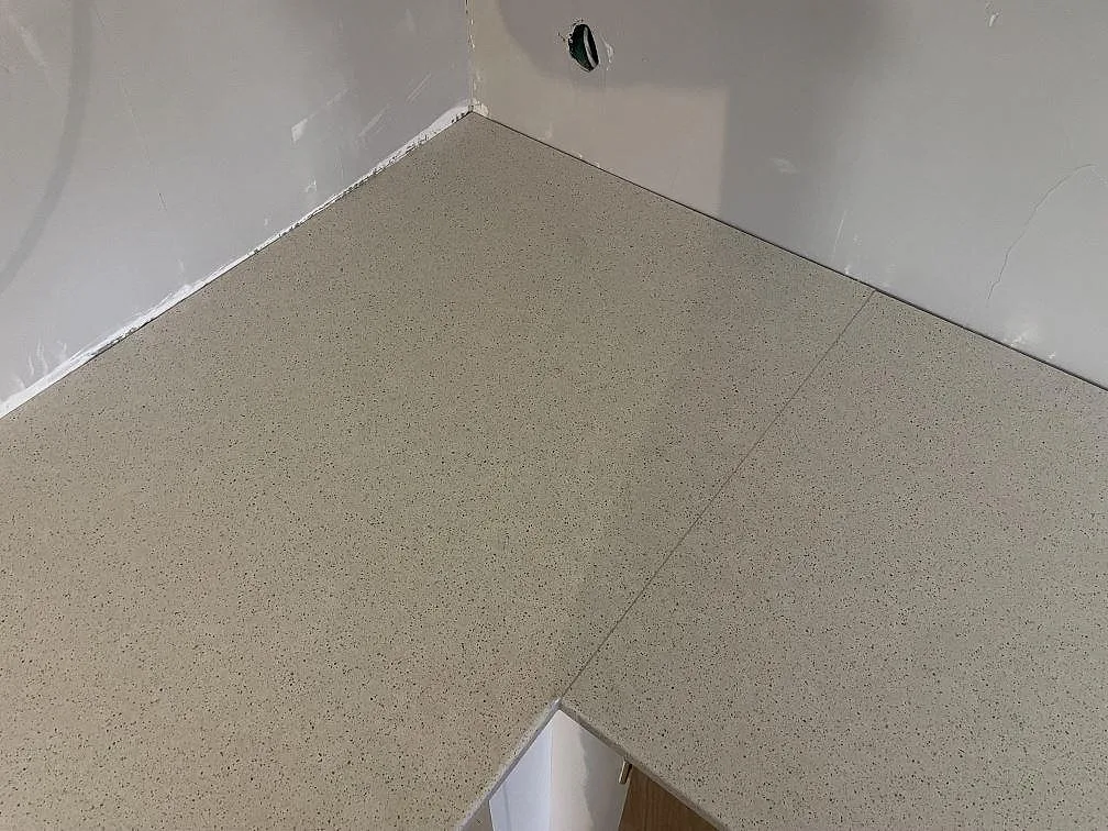 Närbild av L-formad köksbänkskiva i polerad Silestone Blanco City med skarv och specklad kvartskomposit i Hässelby.