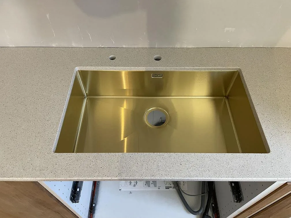 Detalj av polerad Silestone Blanco City runt en rostfri diskho och kranhål i ett kök i Hässelby.