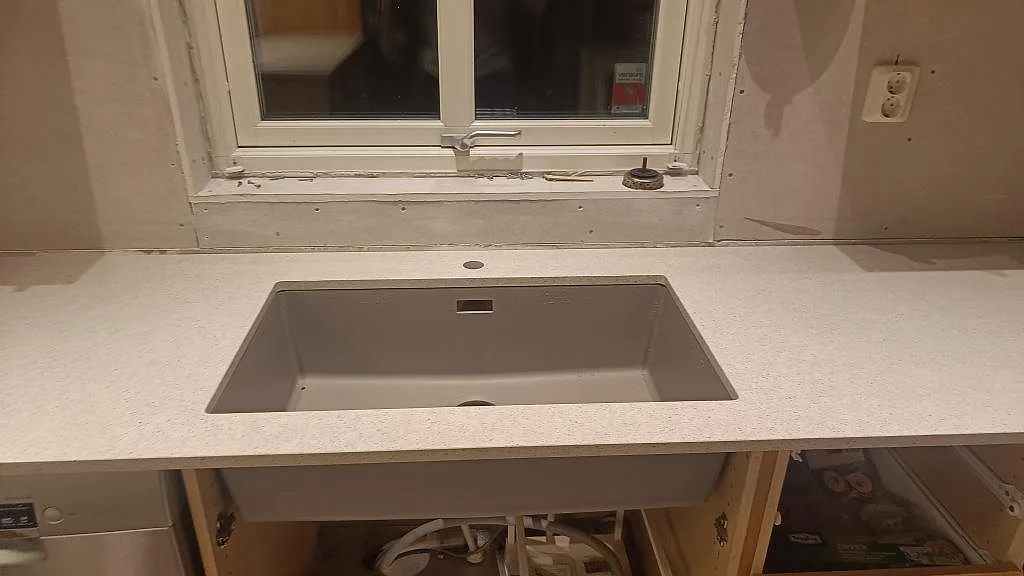 Köksbänkskiva i polerad Silestone Blanco City komposit runt en diskho under fönster i Malmö.