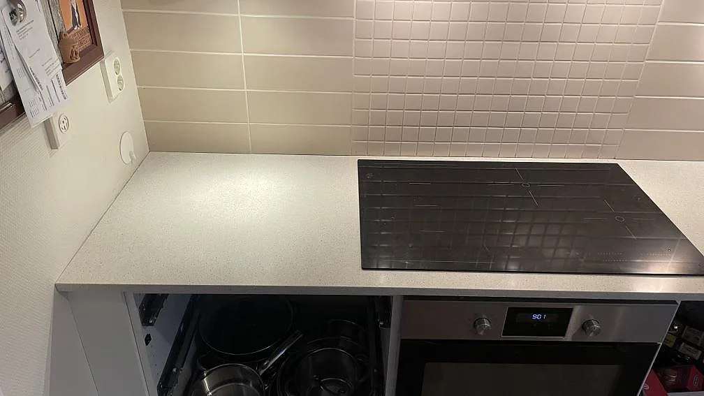 Polerad köksbänkskiva i Silestone Blanco City vid en svart häll mot kaklad vägg i ett kök i Tygelsjö.