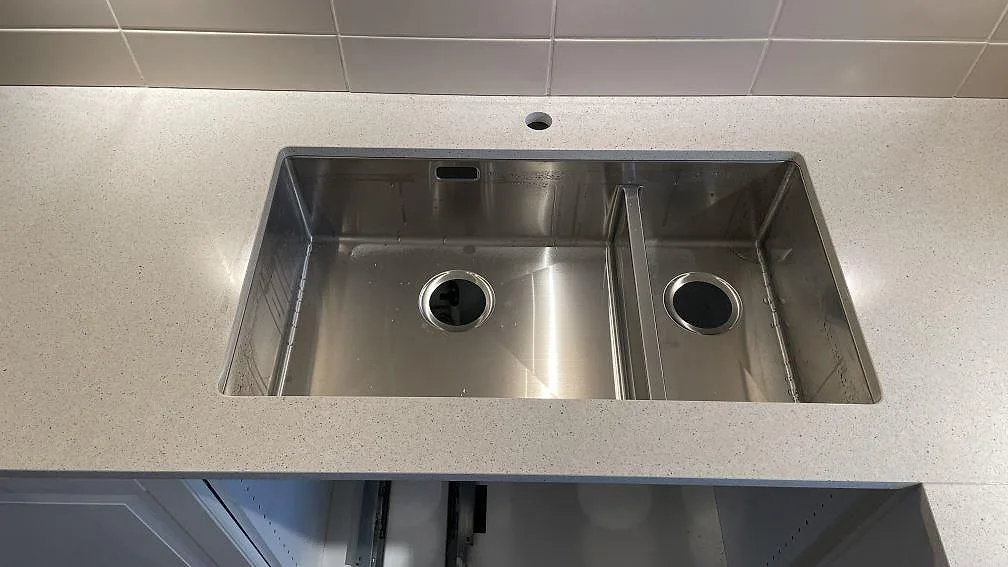 Rostfri dubbelho ovanpå en polerad Silestone Blanco City köksbänkskiva med borrat blandarhål i ett kök i Tygelsjö.