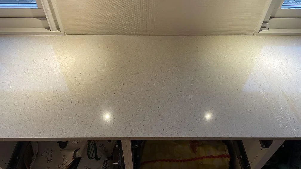 Lång köksbänkskiva i polerad Silestone Blanco City under fönster med ljusreflexer i ett kök i Tygelsjö.