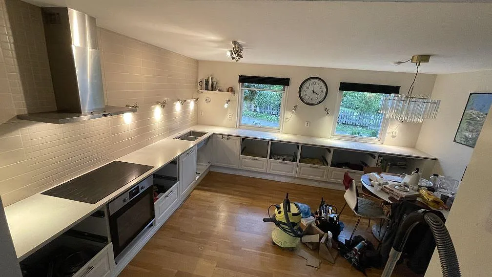 Köksbänkskivor i Silestone Blanco City, polerad ljus kvartskomposit, med häll, rostfri diskho och långa bänkar under fönster i ett kök i Tygelsjö.