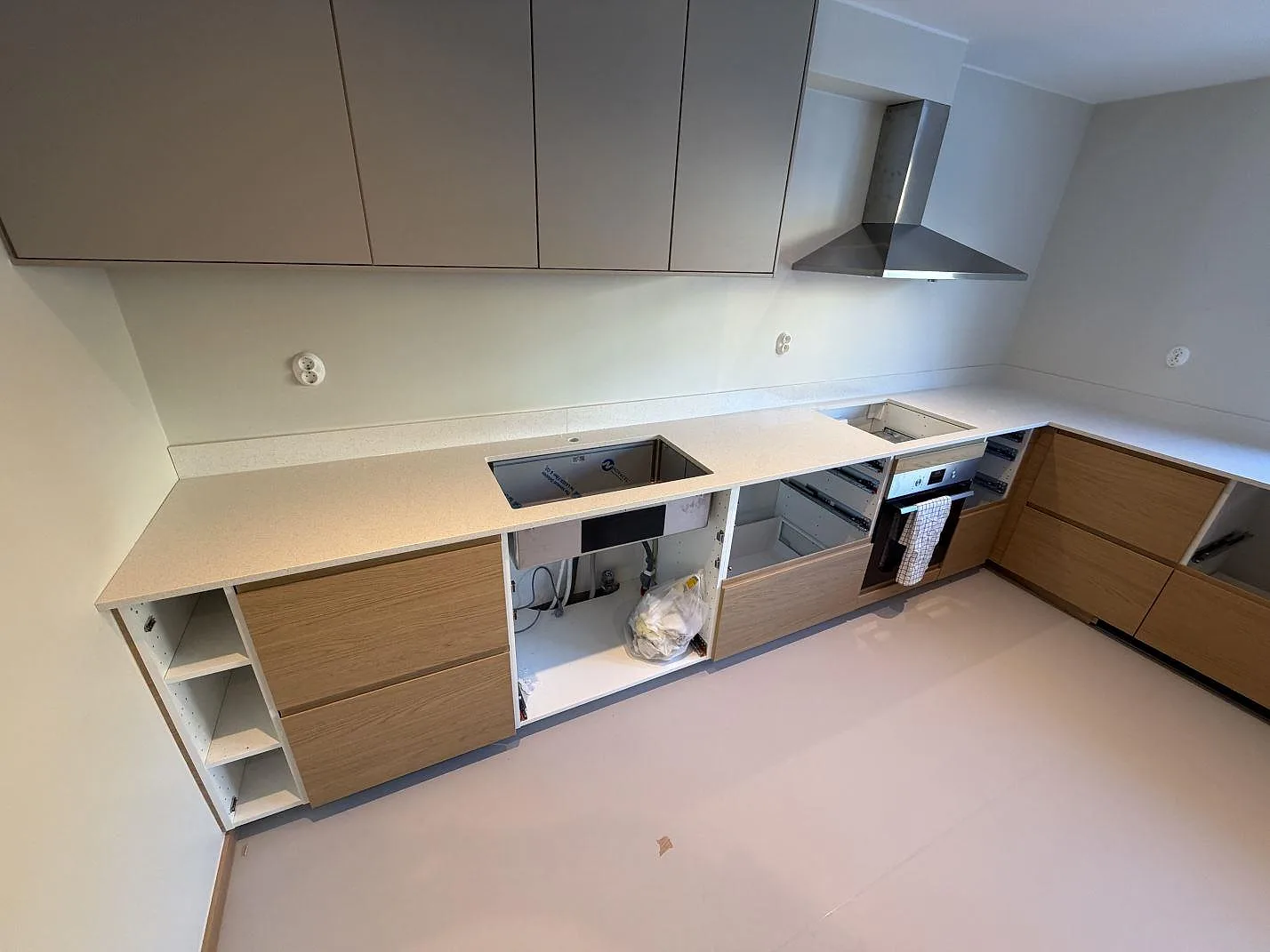 Köksbänkskiva i krämvit Silestone Blanco Maple 14, polerad, med underlimmad diskho och urtag för häll i ett L-format kök under montering i Hässelby.