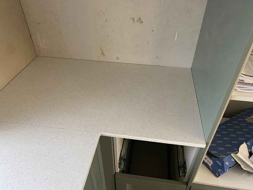 Hörnsektion med köksbänkskiva i polerad Silestone Blanco Maple 14 ovanpå gröna köksstommar i Klagshamn.