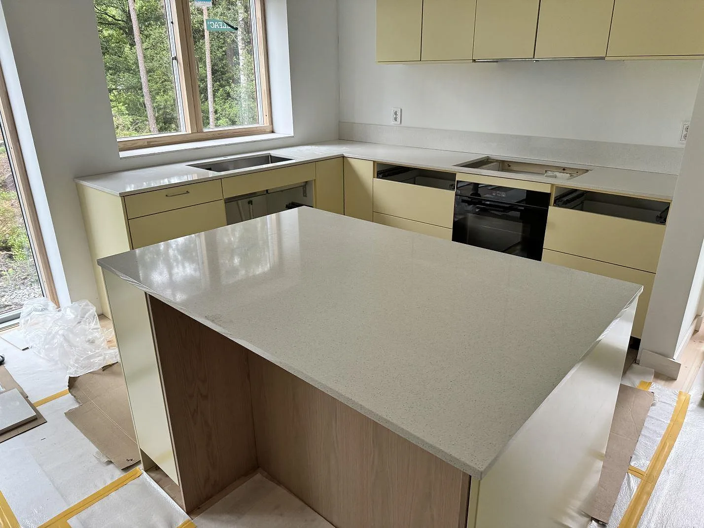 Köksbänkskiva och köksö i krämvit Silestone Blanco Maple 14, polerad kvartskomposit, med underlimmad rostfri dubbelho och hällurtagning i ett kök i Lerum.