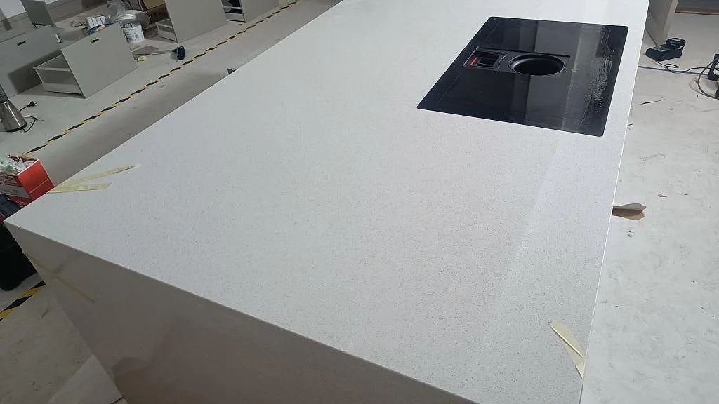 Närbild på ljus polerad Silestone Blanco Maple 14 med svart häll och stor arbetsyta på köksö i Lund.