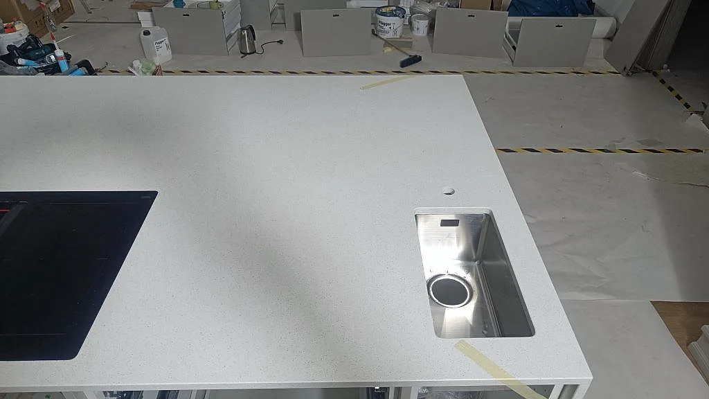 Polerad köksbänkskiva i Silestone Blanco Maple 14 med rostfri diskho, blandarhål och svart häll i ett kök i Lund.