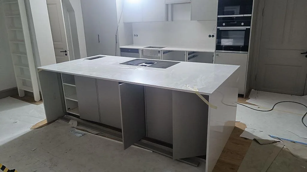 Stor köksö i polerad Silestone Blanco Maple 14 med induktionshäll, bänkrad och vita skåpstommar i ett kök i Lund.