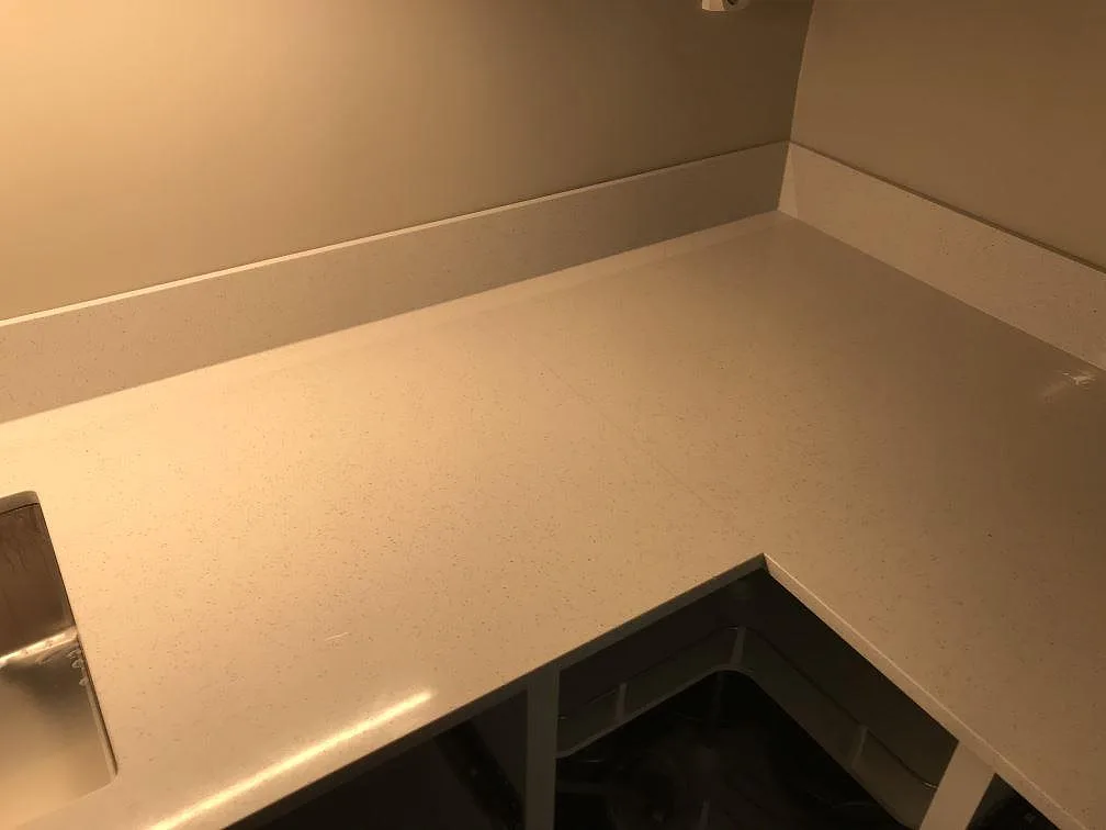 L-formad köksbänkskiva i polerad Silestone Blanco Maple 14 med uppvikt stänkkant under montering i Malmö.