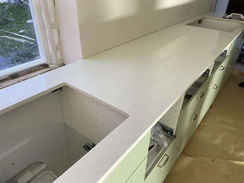 Polerad köksbänkskiva i Silestone Blanco Maple 14 med två förberedda urtag längs fönsterväggen i ett kök under montering i Malmö.