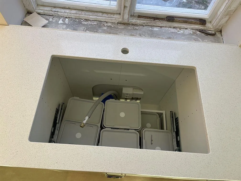 Underlimmat diskhourtag och kranhål i polerad Silestone Blanco Maple 14 framför ett fönster i ett kök under montering i Malmö.
