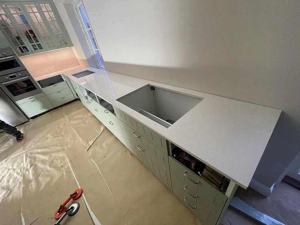 L-formad köksbänkskiva i polerad Silestone Blanco Maple 14, vit kvartskomposit med underlimmat diskhourtag och hällurtag i ett kök i Malmö.