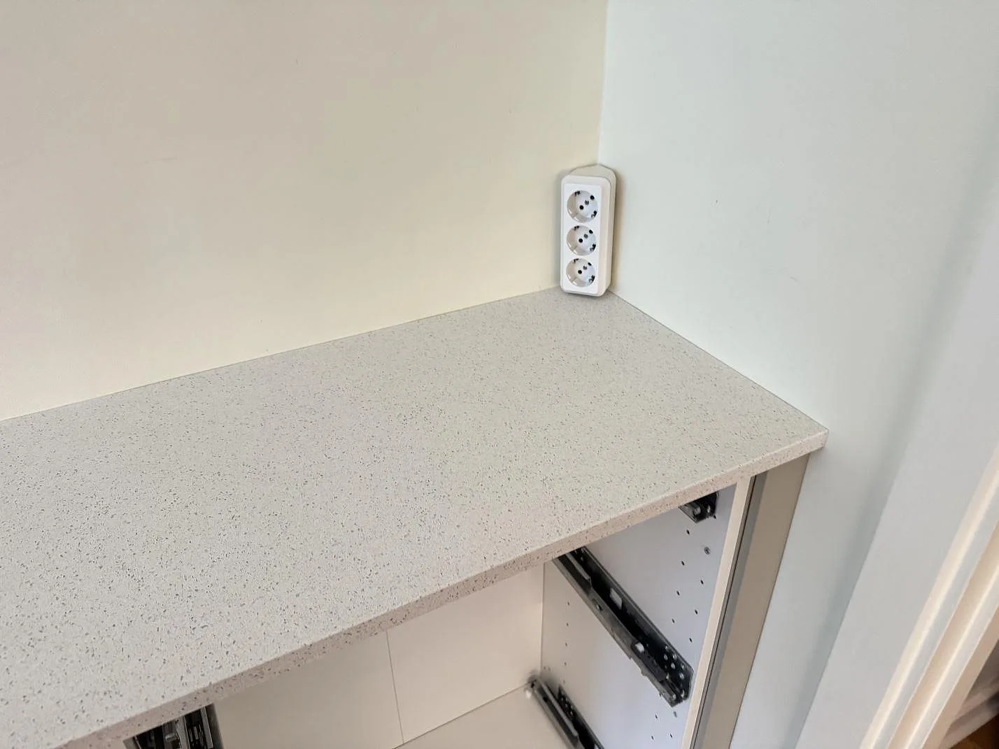 Detalj av finkornig Silestone Blanco Maple 14 bänkskiva, polerad, vid vägguttag och öppna köksstommar i Malmö.