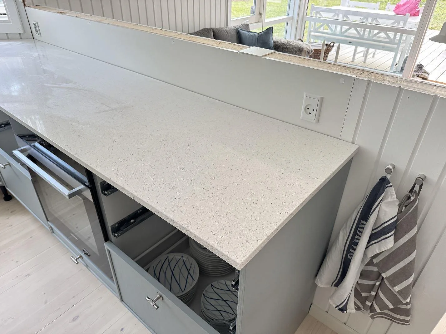 Köksbänkskiva i ljus Silestone Blanco Maple 14, polerad kvartskomposit, längs en lång rak bänk med öppna stommar under montering i ett kök i Rørvig.