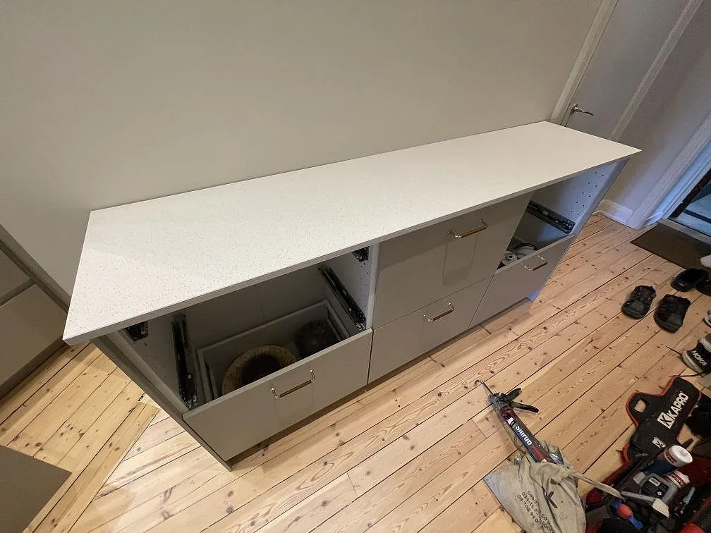Köksbänkskiva i vit polerad Silestone Blanco Maple 14, kvartskomposit, på grå köksstommar under montering i Stockholm.