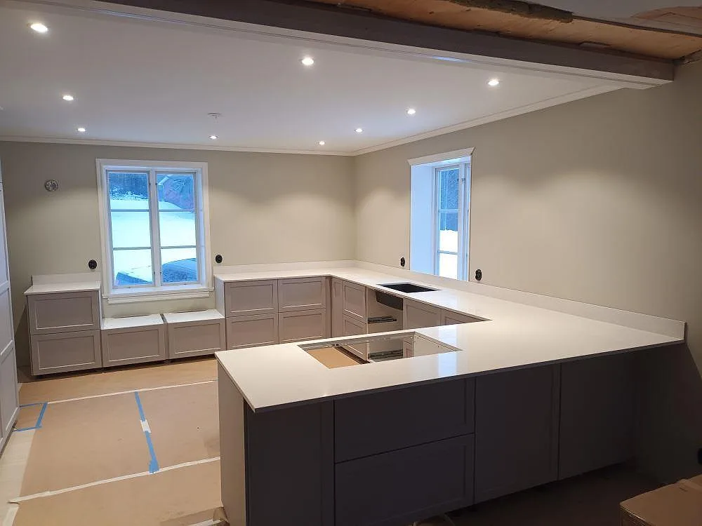 Köksbänkskiva i ljus Silestone Blanco Maple, polerad, i ett U-format kök i Toftbyn med underlimmad diskho på bakre bänken och urtagning för häll i köksön.