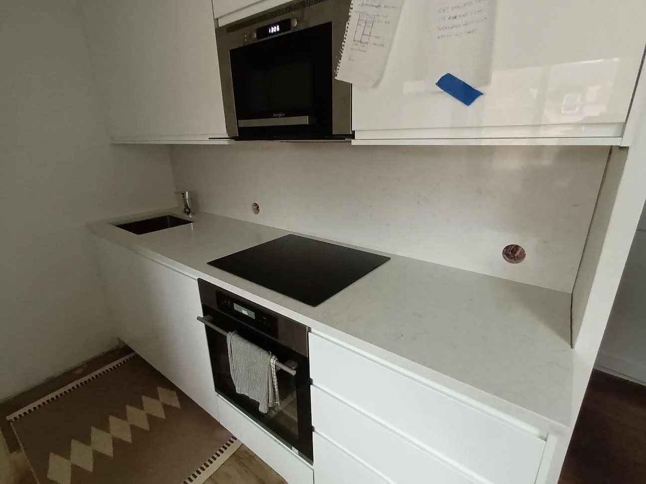 Köksbänkskiva i vit Silestone Blanco Orion, polerad, med underlimmad diskho, infälld induktionshäll och uppvikt stänkskydd i ett kök i Danderyd.