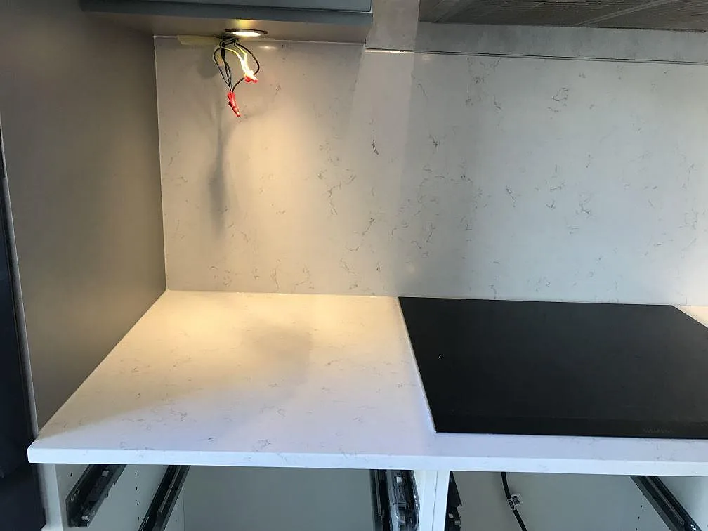 Bänkrad och heltäckande stänkvägg i Silestone Blanco Orion med infälld svart induktionshäll i ett kök i Jönköping.